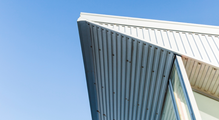 Low-angle view of a modern roof overhang featuring corrugated metal siding and roof paneling against a clear blue sky, installed by Stahl Roofing.